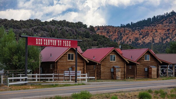 A log cabin hotel with a red roof, a sign reading 'Red Canyon RV Park,' and a sign for 'Trophy Hoops Disc Golf.' - Red Canyon Village (Panguitch)