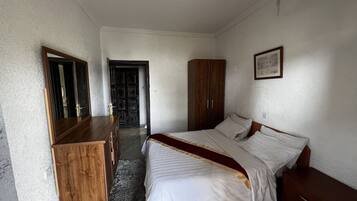 A bedroom with a bed, a wooden dresser, a wardrobe, and a framed picture on the wall.