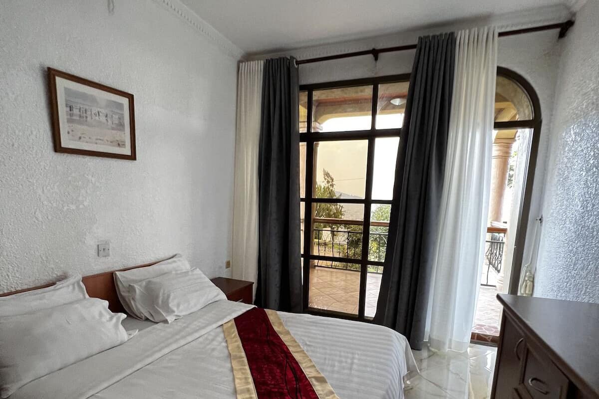 Une chambre d’hôtel avec un lit, une commode, un tableau encadré au mur et une fenêtre avec des rideaux.