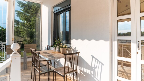A covered patio with a table and chairs, a window, and a door with glass panels. - Hebe's house | Cozy Village Escape Near Tripoli (Stadio)