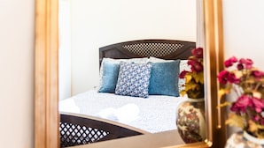 A bed with a patterned bedspread and pillows, a wooden headboard, and a vase with flowers. - Hebe's house | Cozy Village Escape Near Tripoli (Stadio)