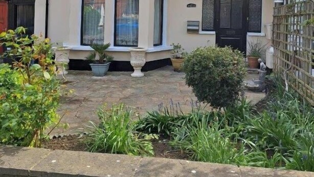 Een tweelaags huis met een erker, een voordeur en een kleine tuin met potplanten.