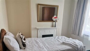 Een hotelkamer met een bed, een witte schoorsteen, een spiegel boven de schoorsteen en een raam met gordijnen.