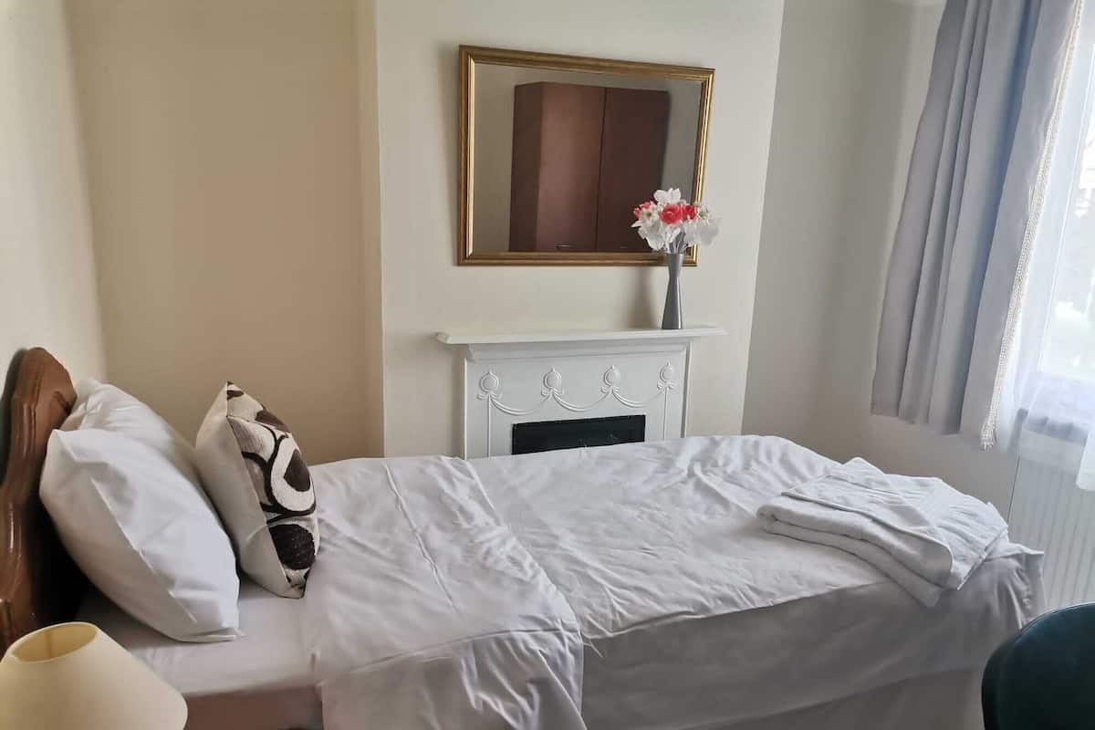 Une chambre d’hôtel avec un lit, une cheminée blanche, un miroir au-dessus de la cheminée et une fenêtre avec des rideaux.