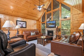 A log cabin interior with a fireplace, leather furniture, a television, and a ceiling fan. - New Listing, Game Room. Hot Tub, Pool Access +Free Attractions! (Sevierville)