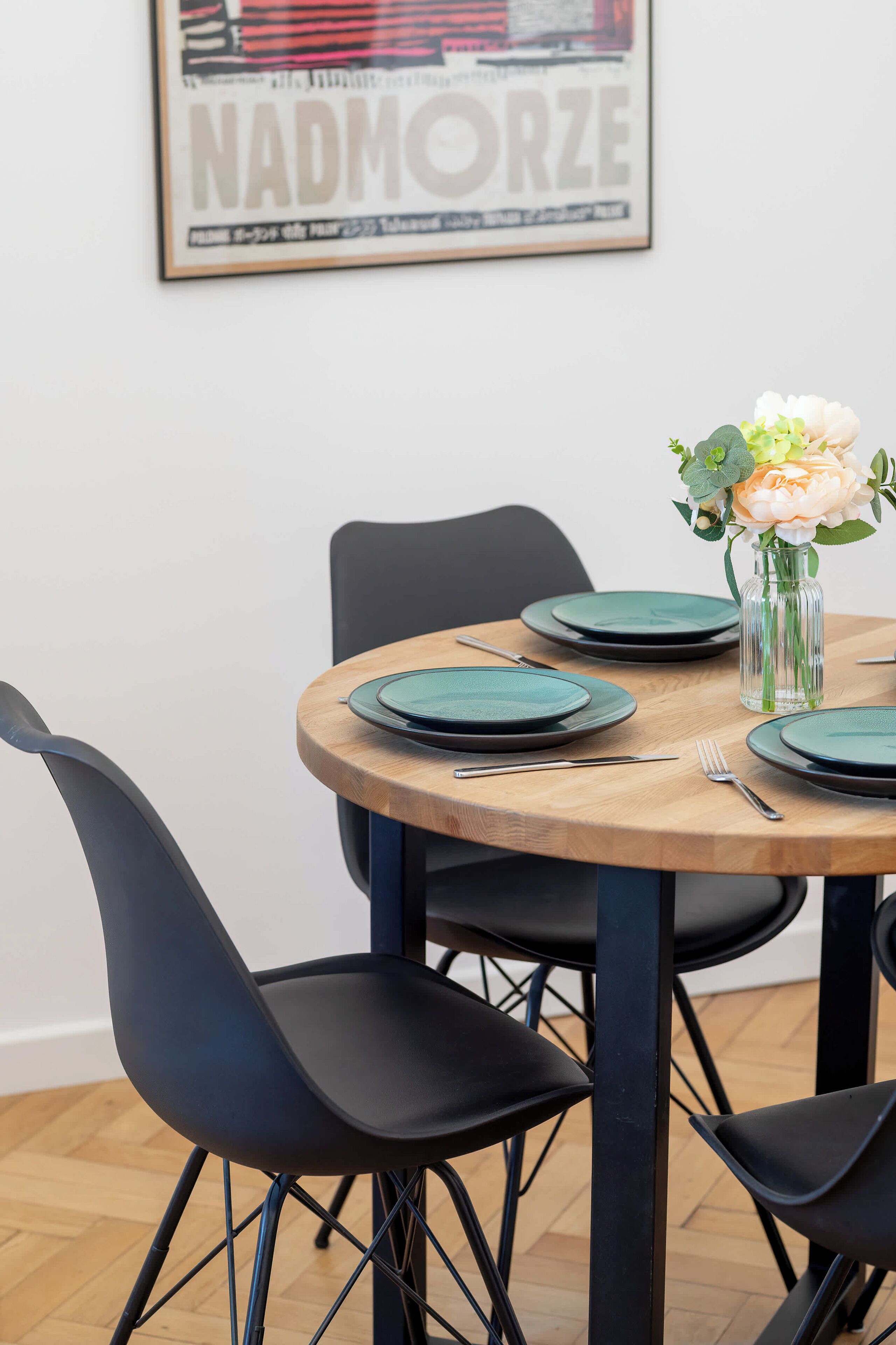 Une table à manger avec des assiettes vertes, un vase rempli de fleurs et des chaises noires.