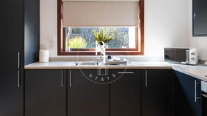 A modern kitchen with a built-in microwave, a sink with a faucet, and a window with a view of greenery. - The Den on Hay Crescent (Peterhead)