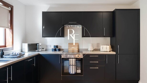 A modern kitchen with black cabinets, a microwave, a toaster, and a kettle. - The Den on Hay Crescent (Peterhead)