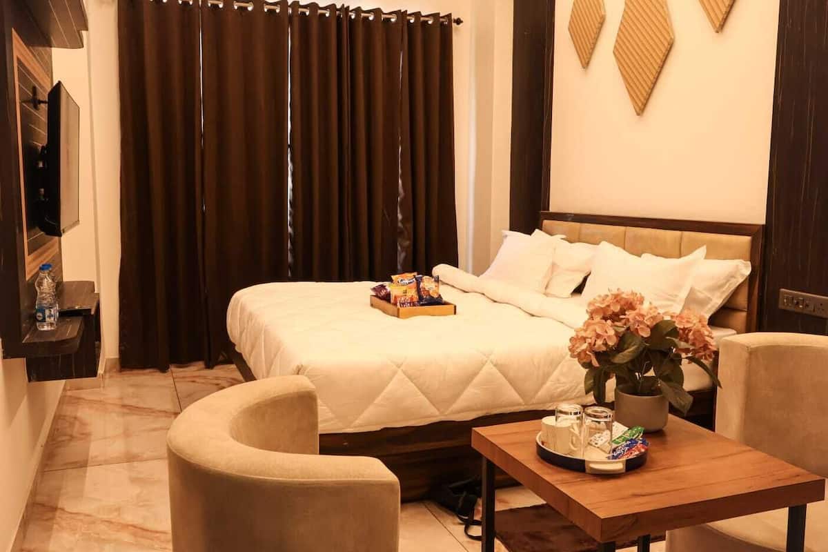 Una habitación de hotel con una cama, una mesita de noche con aperitivos, una silla, un televisor y cortinas.