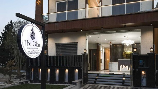 A modern hotel entrance with a sign, a covered outdoor area, and a well-lit interior. - The Glam By Sandane Homes (Greater Noida)