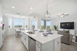 A modern kitchen with a central island, white cabinetry, and a dining area with a table and chairs. - Wellen Park G&CC - 2 bed 2 bath with golf (Venice)