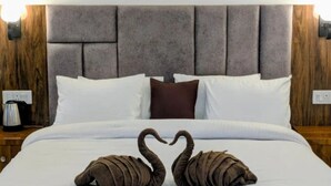 Ein Bett mit grauem gepolsterten Kopfteil, weißer Bettwäsche, einem braunen Kopfkissen und zwei schwanenförmigen Handtüchern.