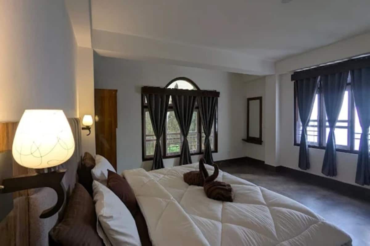 A hotel room with a bed, a lamp, curtains, and a window.