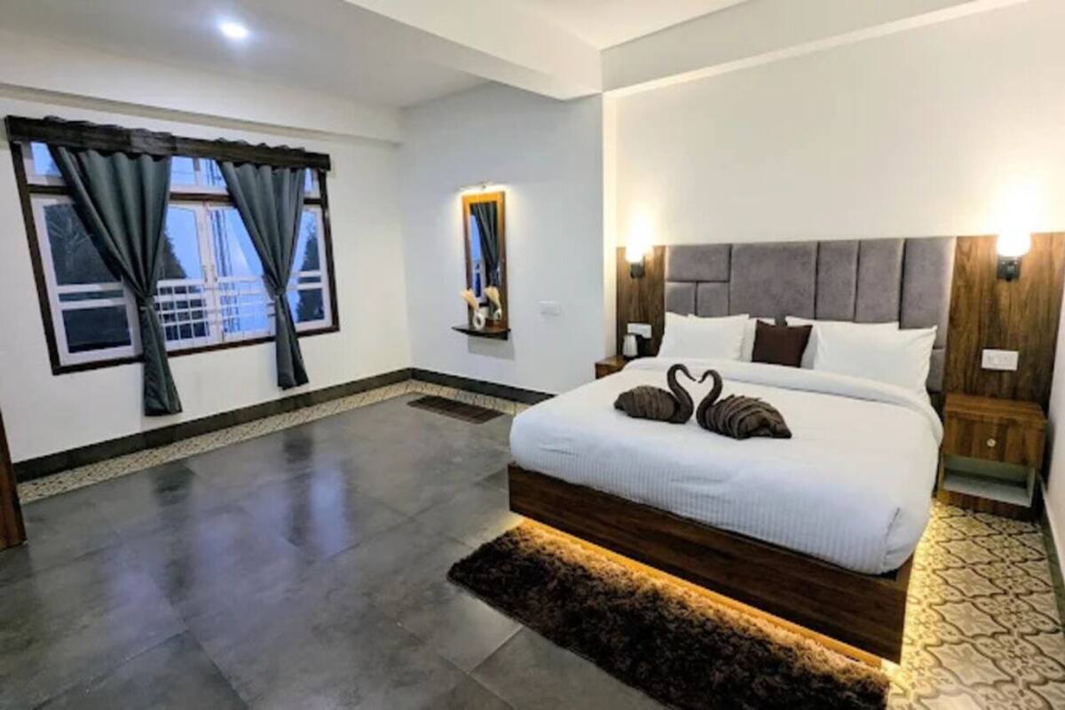 A modern bedroom with a large bed, a nightstand, a mirror, and a window with curtains.