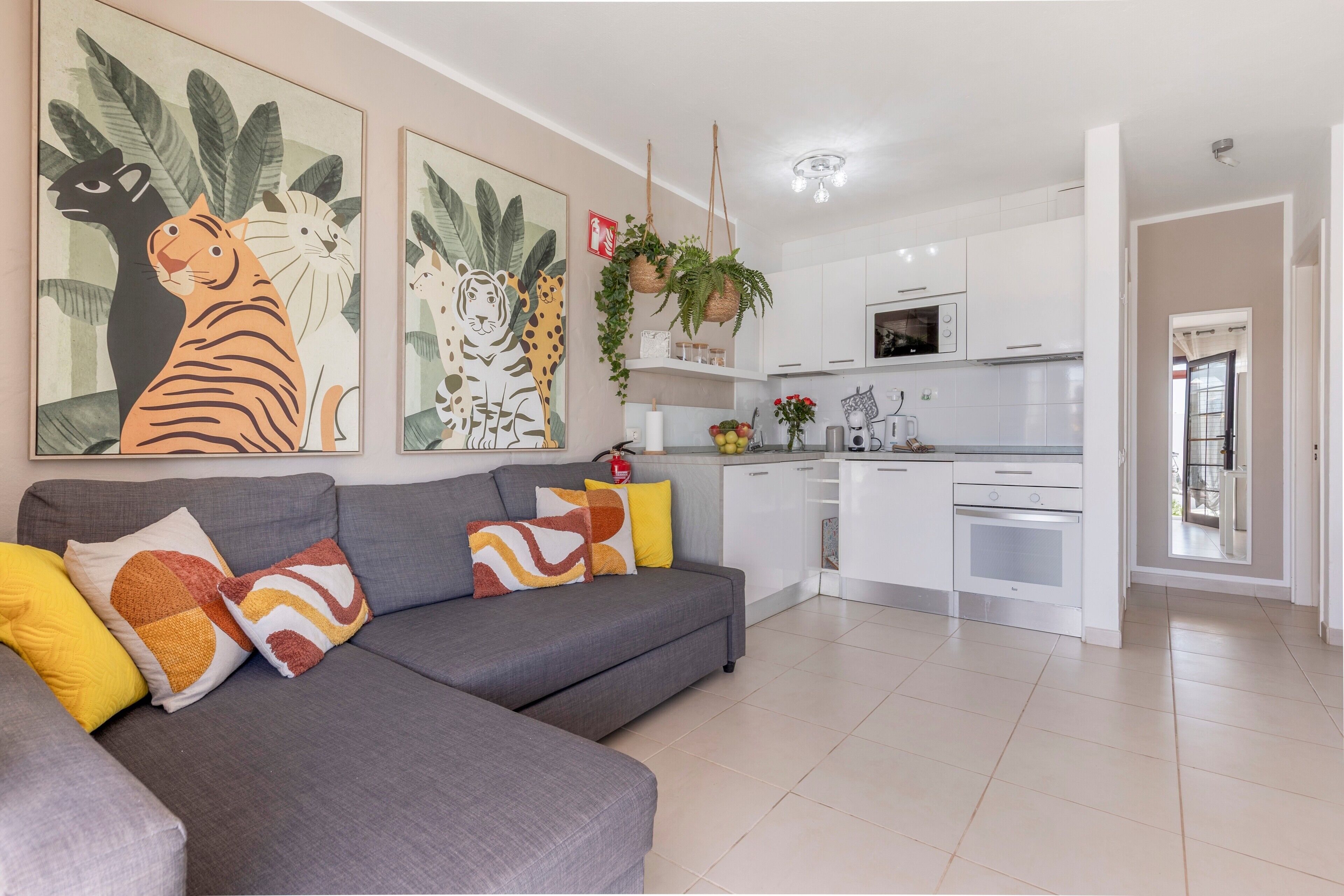 Een moderne woonkamer met een grijze bank, kleurrijke kussens en twee grote dierenportretten aan de muur.