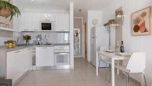 Eine moderne Küche mit weißen Schränken, ein Essbereich mit einem weißen Tisch und Stühlen sowie ein Kühlschrank.