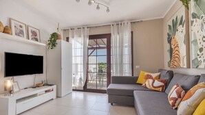 Ein modernes Wohnzimmer mit Flachbildfernseher, weißem Unterhaltungsmöbel, grauem Sofa und farbenfrohen Kissen.