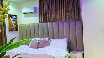 A modern bedroom with a bed, bedside tables, a wall-mounted air conditioner, and a ceiling with blue lighting.
