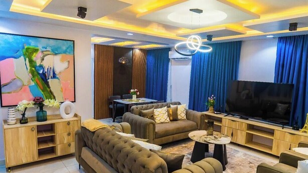 A modern living room with a sofa set, a television, and a dining area. - ELIZ APARTMENT (Osogbo)