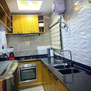 A kitchen with wooden cabinets, a built-in oven, a gas stove, a sink, and a water heater. - ELIZ APARTMENT (Osogbo)