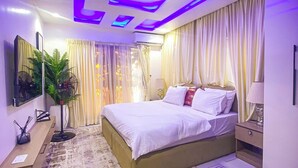 A modern bedroom with a bed, bedside tables, a mirror, curtains, and a ceiling with recessed lighting. - ELIZ APARTMENT (Osogbo)