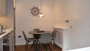 A compact kitchen with a dining area, a ship's wheel decoration, and a white door. - Riverside House, Lancaster (Lancaster)
