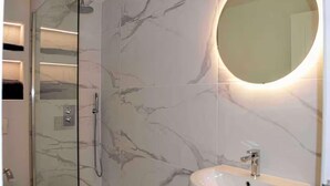 A bathroom with a glass shower enclosure, a marble-tiled wall, and a round mirror. - Riverside House, Lancaster (Lancaster)