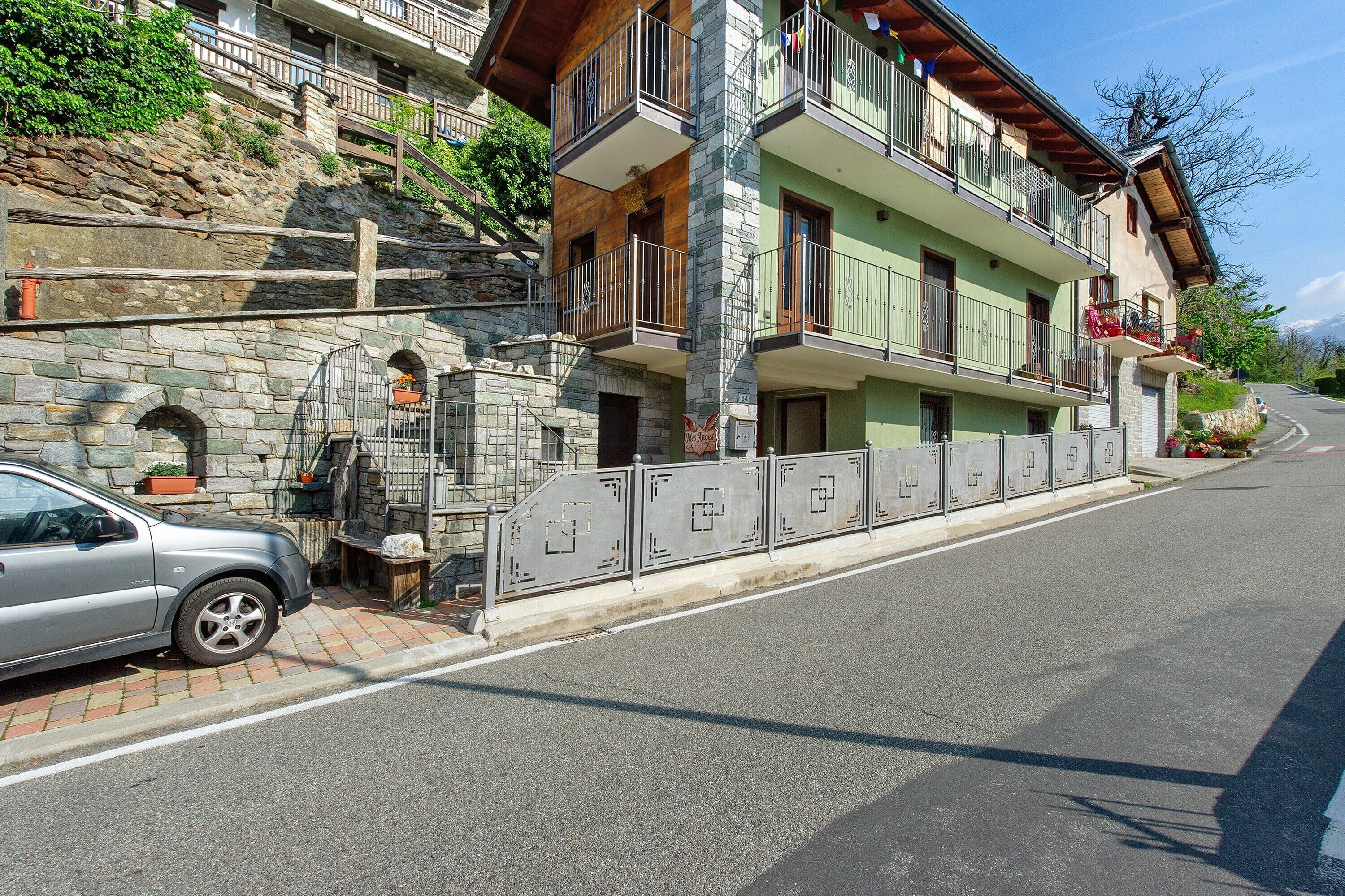 Um edifício de vários andares com varandas, paredes de pedra e um carro estacionado.