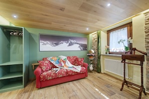 A room with a wooden ceiling, a red floral sofa, a large framed picture, a radiator, and a window with a view.