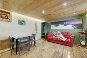 A room with a wooden ceiling, a dining table with chairs, a red sofa, and a large framed picture on the wall.