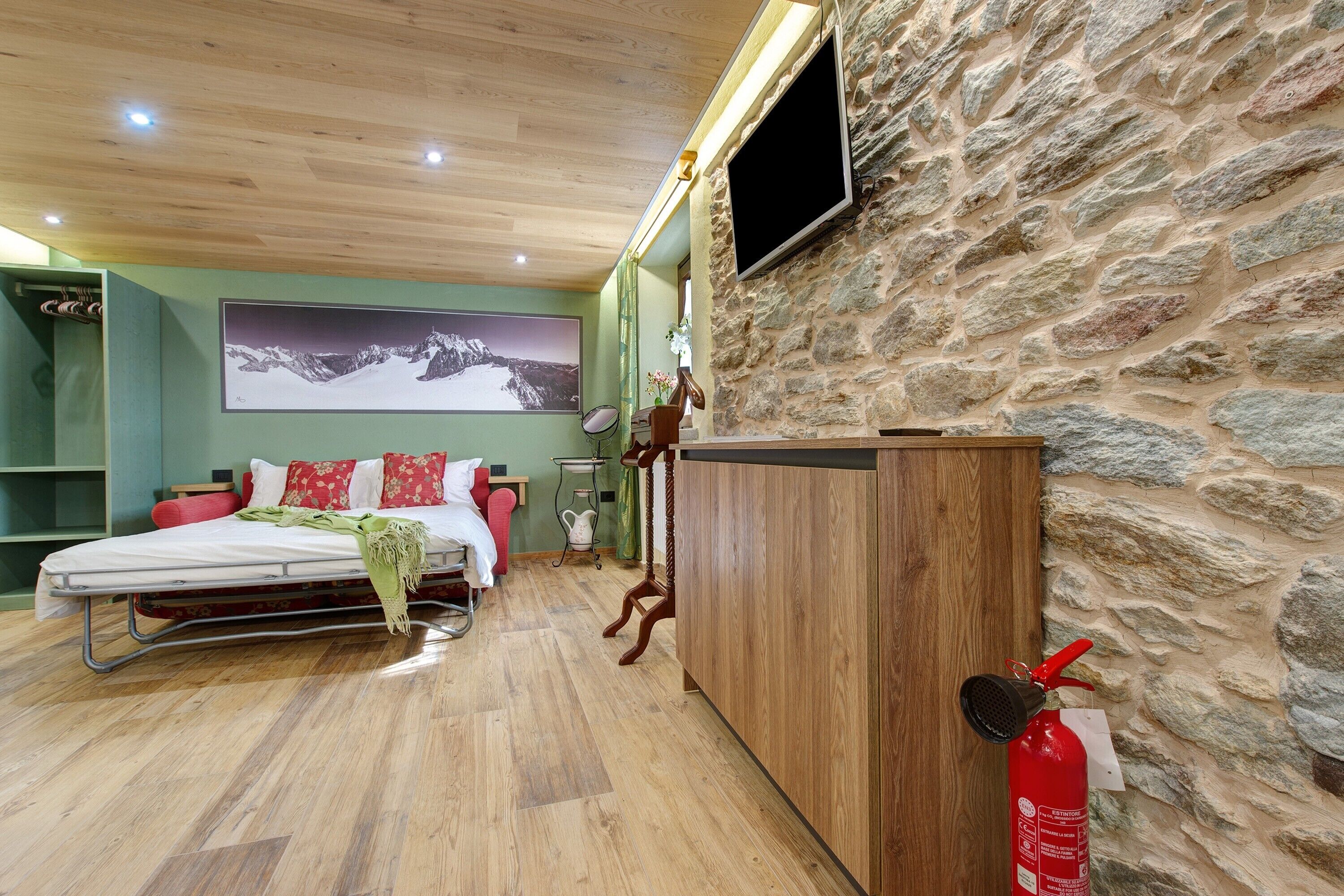 Une chambre à coucher avec un lit, une armoire en bois, un téléviseur fixé au mur et un mur en pierre.