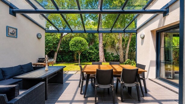 An outdoor patio with a wooden table and chairs, a sofa, and a grill. - Villa 'Le Rêve' in Mimizan Plage with Terrace, Garden, and Air Conditioning (Mimizan)