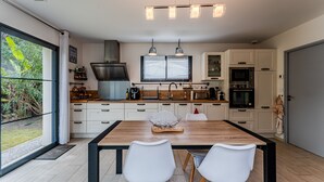 A modern kitchen with a wooden table, white chairs, a black range hood, and built-in appliances. - Villa 'Le Rêve' in Mimizan Plage with Terrace, Garden, and Air Conditioning (Mimizan)
