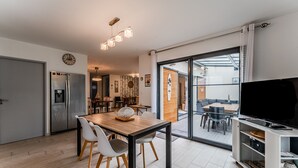 A modern kitchen with a refrigerator, dining table with chairs, and a TV on a stand. - Villa 'Le Rêve' in Mimizan Plage with Terrace, Garden, and Air Conditioning (Mimizan)