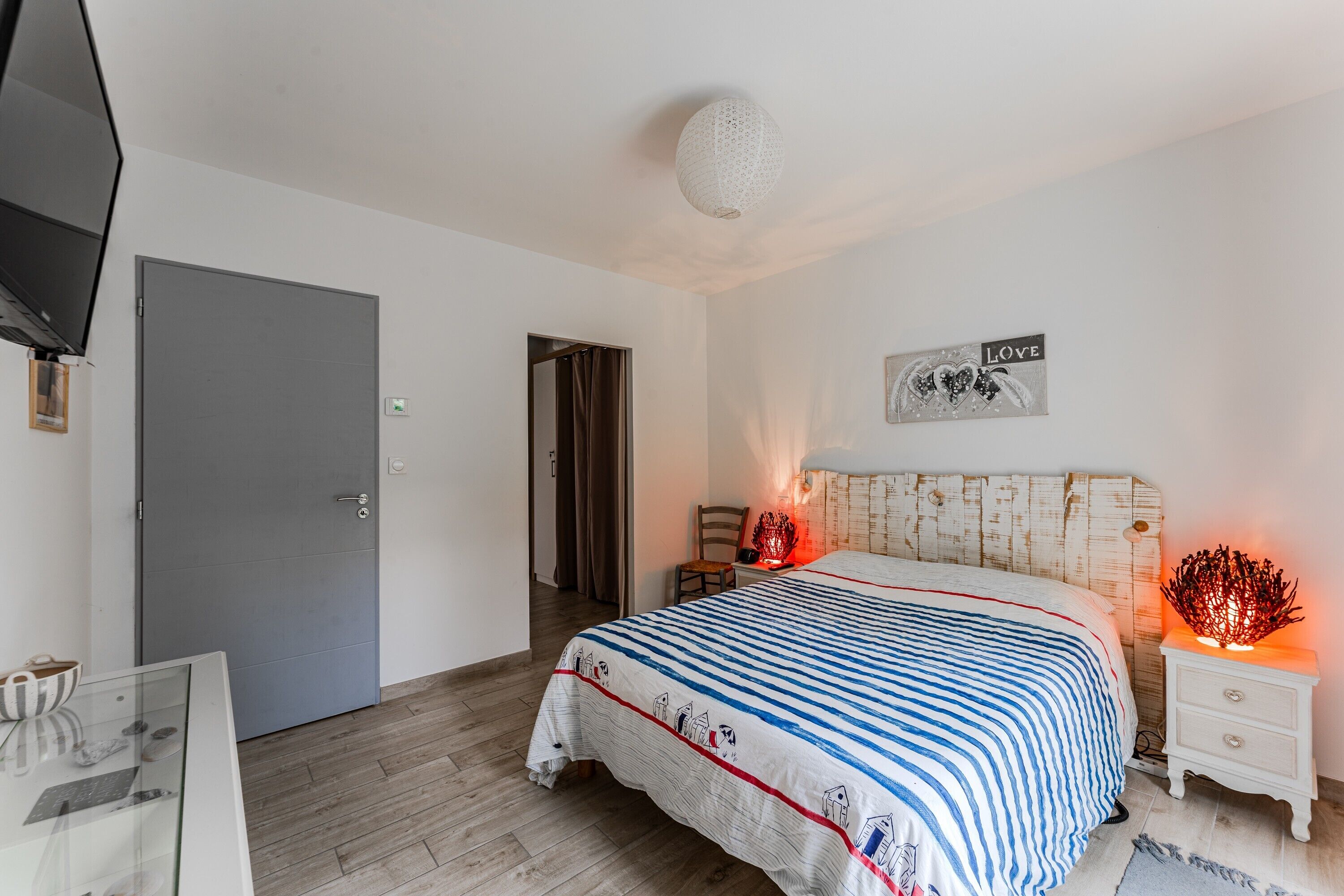 A bedroom with a bed, bedside tables, a television, a door, and a wall with a 'LOVE' sign.