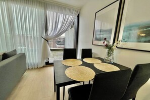 Ein Essbereich mit Tisch für vier Personen, einer Couch und einem großen Fenster mit transparenten Vorhängen.