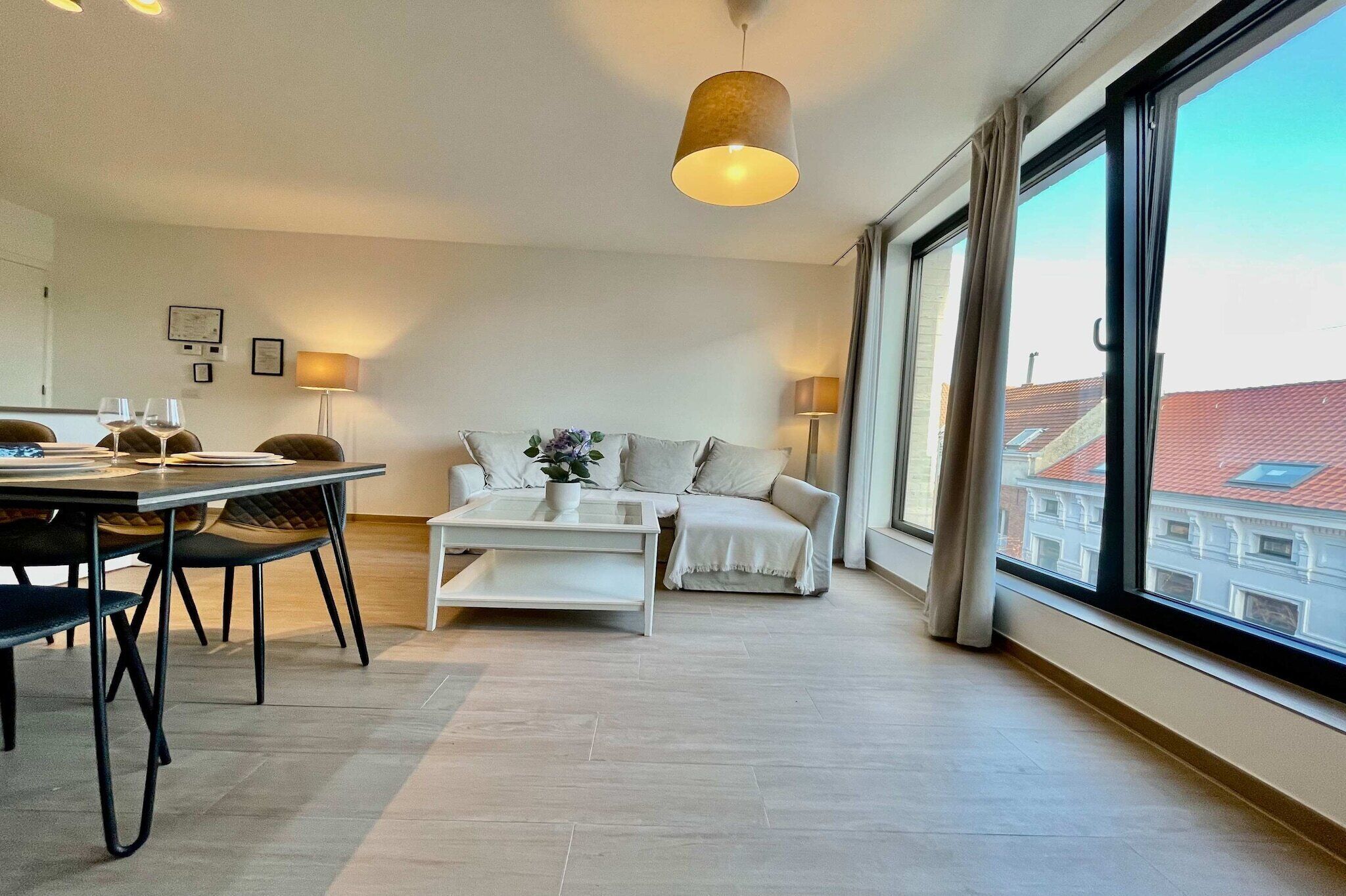 Una sala de estar moderna con comedor, un sofá, una mesa de centro y un amplio ventanal con cortinas.