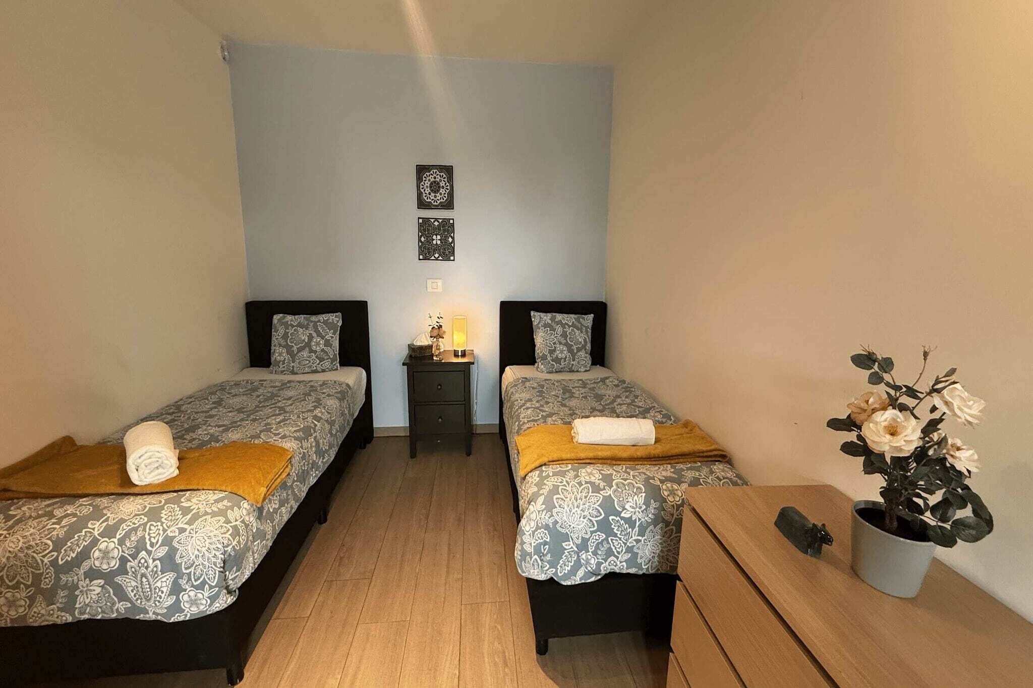 Ein Zimmer mit zwei Betten, einem kleinen Tisch, einem Nachttisch und einer Topfpflanze.