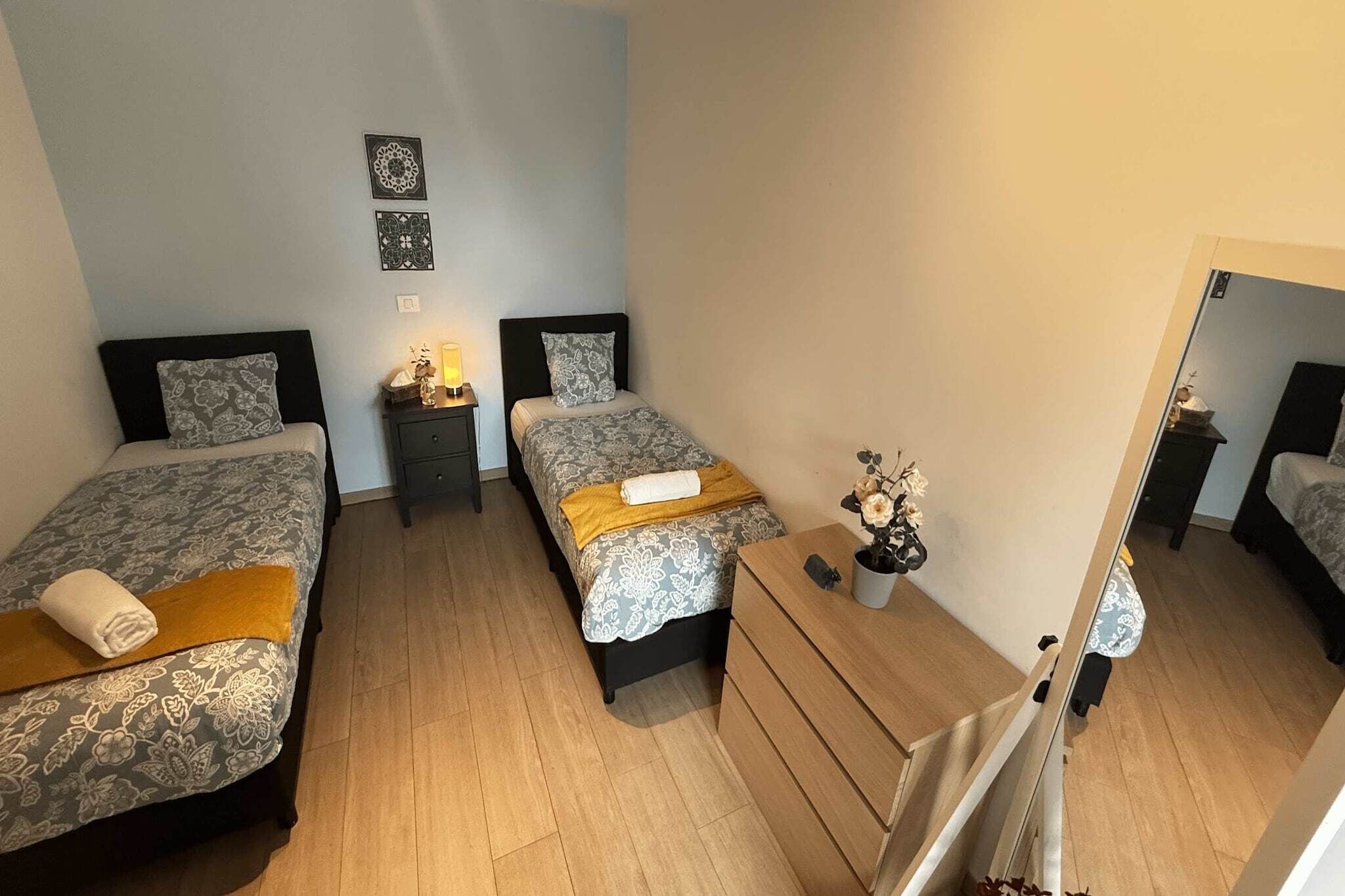 Een slaapkamer met twee bedden, een nachtkastje, een dressoir en een spiegel.