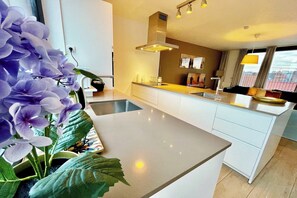 Une cuisine moderne dotée d’un îlot central, d’un four encastré et d’une grande fenêtre avec des rideaux.