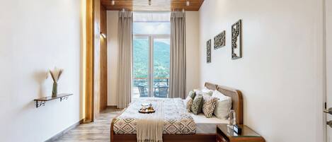 A bedroom with a bed, bedside table, nightstand, and a view of the outdoors.