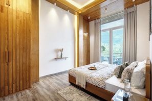 A bedroom with a wooden wardrobe, a bed with patterned bedding, a bedside table with a glass, and a view of greenery outside. - ELIVAAS Antarmann Casa Mirage 3BHK Villa (Bhimtal)