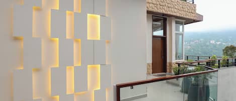 Un edificio moderno con un diseño luminoso geométrico en la pared, un balcón con barandillas de vidrio y una vista de un paisaje lejano.