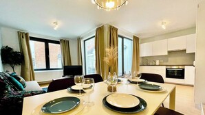 Un espace de repas moderne avec une table dressée pour quatre personnes, un canapé et une cuisine en arrière-plan.