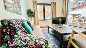 Un salon avec un canapé, une table basse, un téléviseur, une plante et une vue sur un balcon.