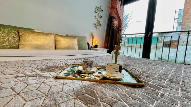 A hotel room with a bed, a tray with cups and a vase, and a view of a building and water outside. - Antwerp Retreat with Kosher Kitchen (Antwerpen)