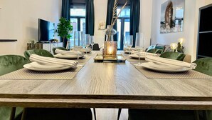 A dining room with a long table set for six, a television, a plant, and a painting on the wall. - Antwerp Retreat with Kosher Kitchen (Antwerpen)