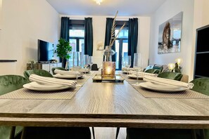 A dining room with a long table set for six, a television, a plant, and a painting on the wall. - Antwerp Retreat with Kosher Kitchen (Antwerpen)