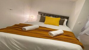 Quarto de hotel com cama, paredes brancas, cabeceira marrom e luminária de cabeceira.