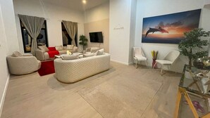 Een moderne woonkamer met een bank, stoelen, een flatscreen televisie en een groot schilderij van een dolfijn.